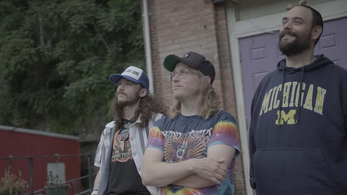 Three members of the Thomas Jude Band outside a brick building